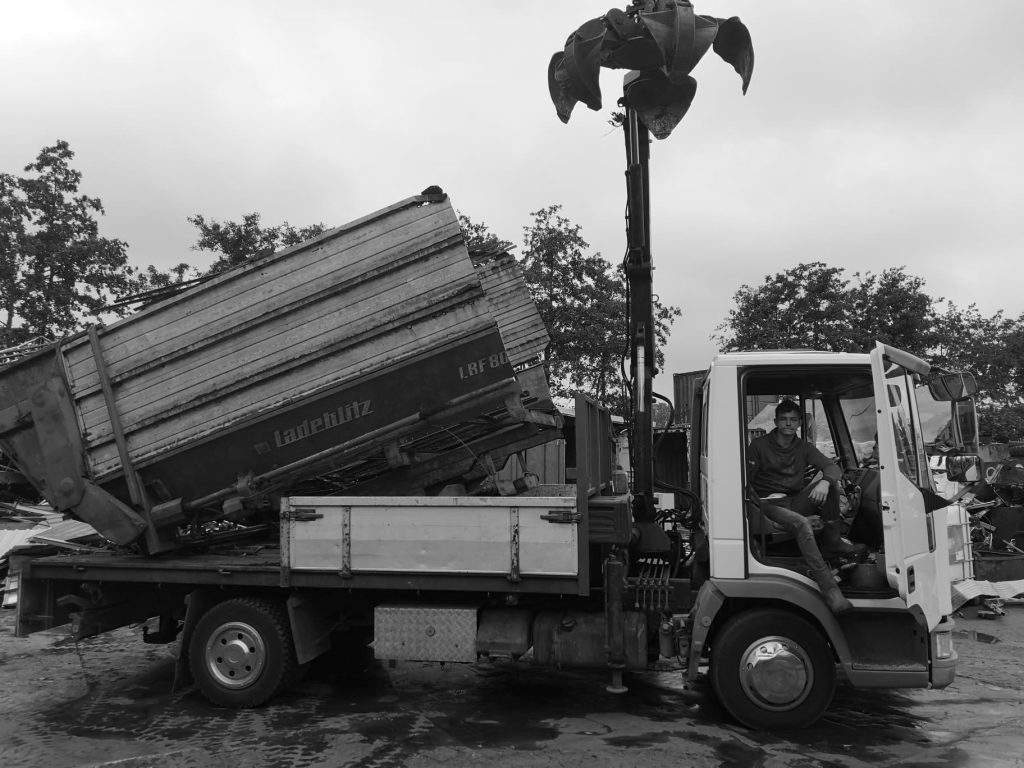 Oude foto van truck om metaal en ijzer mee op te halen met de deur open, de grootvader zit voorin.